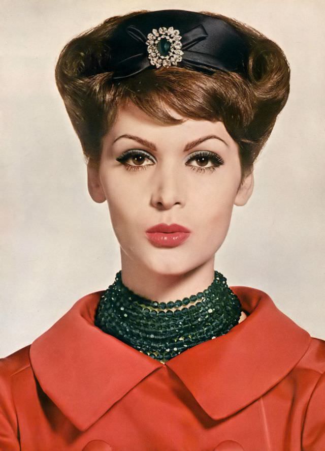 #25 Isabella Albonico is wearing a red satin evening coat, black satin hat, and cut crystal beads of deep sea-green, all by Dior, make-up from Max Factor. Vogue, November 1, 1959