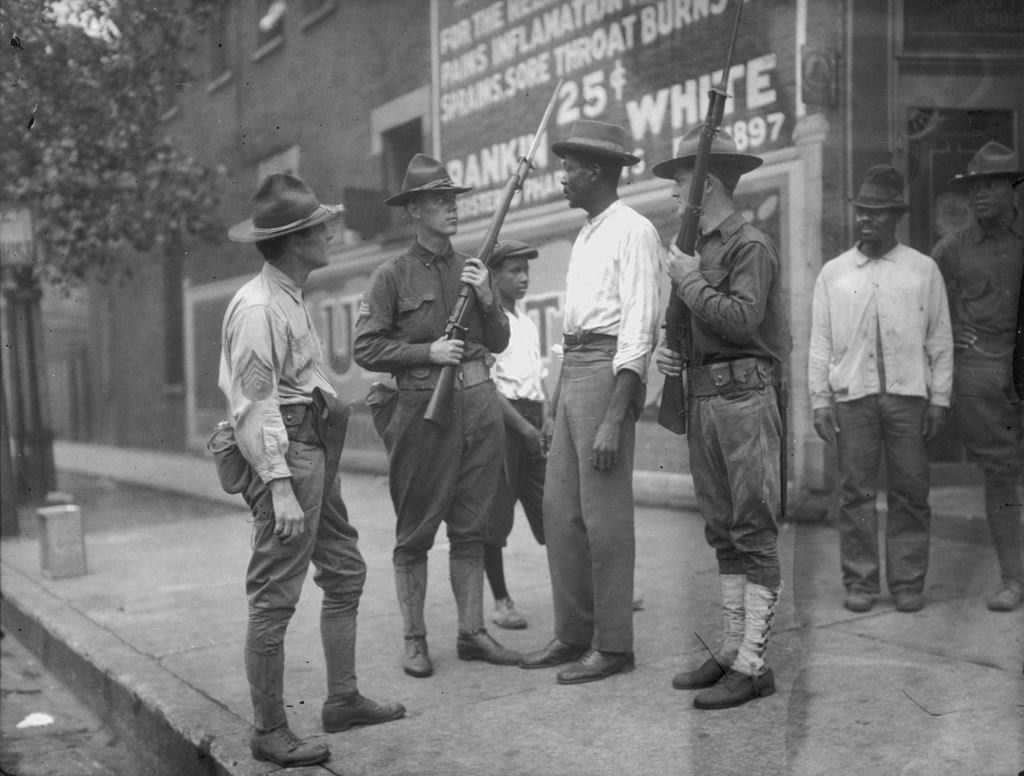 #56 National Guardsmen, called in by Mayor ‘Big Bill’ Thompson after three days of rioting, question an African American man in Chicago, 1919.