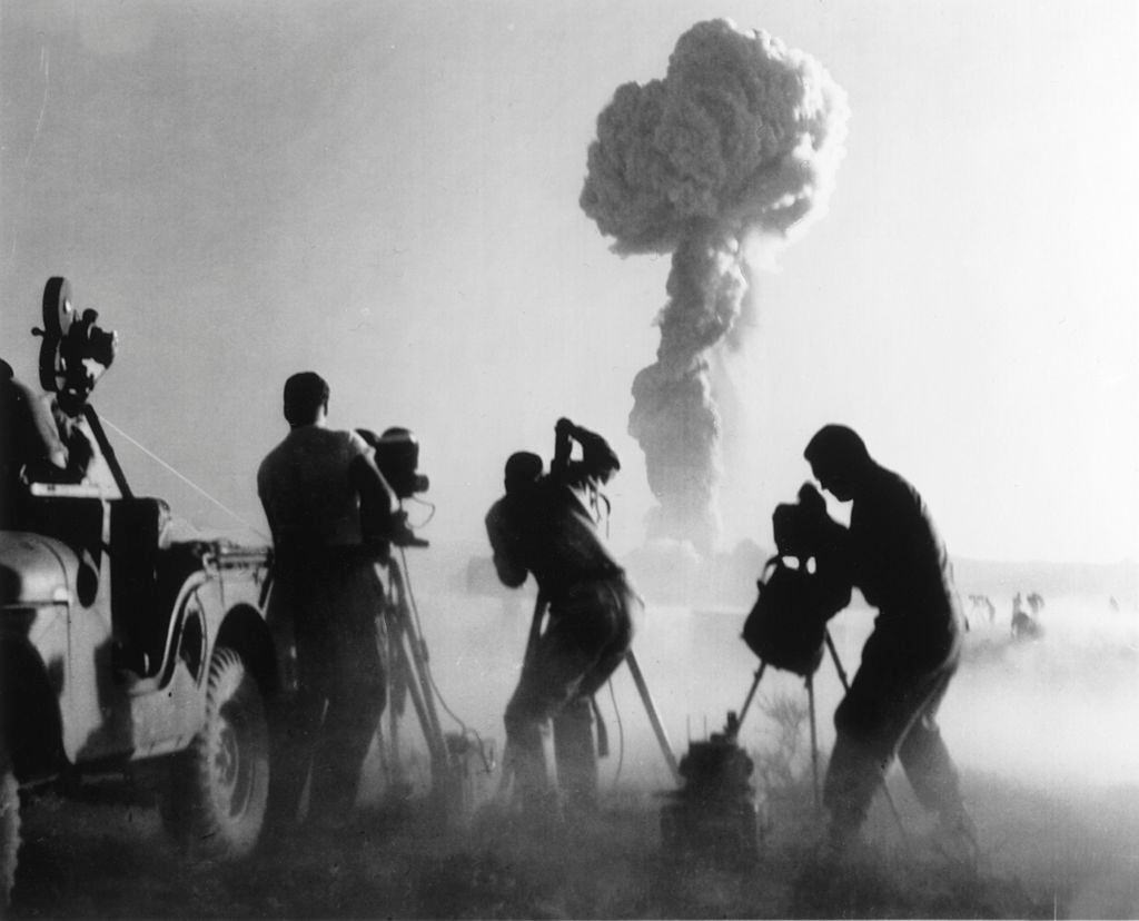 #19 Filmmakers, next to a jeep, capturing an atomic explosion, at a Nevada desert test site, 1957.