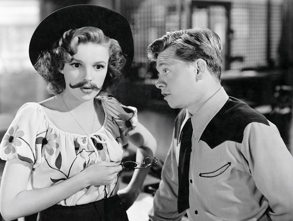 #23 Mickey Rooney and mustachioed and be-hatted Judy Garland confer in the 1943 MGM musical comedy, Girl Crazy.