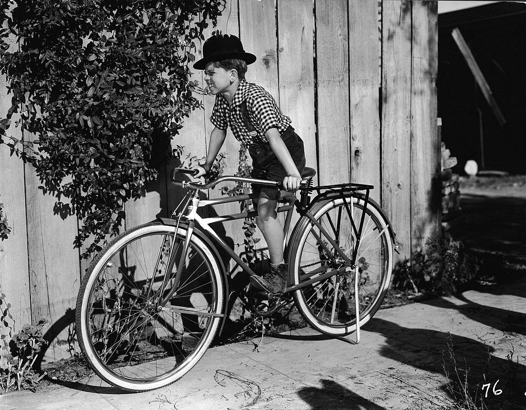 #9 Mickey Rooney ina bowler hat on a bicycle in a film still from one of the numerous ‘Mickey McGuire’ comedy shorts, 1930.