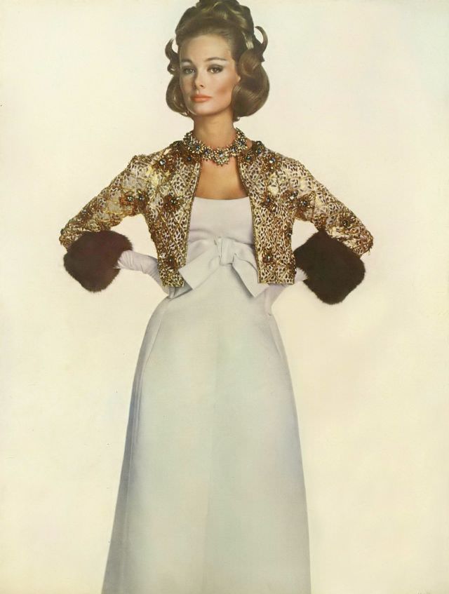 #16 Monique Chevalier in ball gown of white satin, narrow with high bow, and jacket of gold and bronze-colored embroidery cuffed in sable, Vogue. November 1, 1962