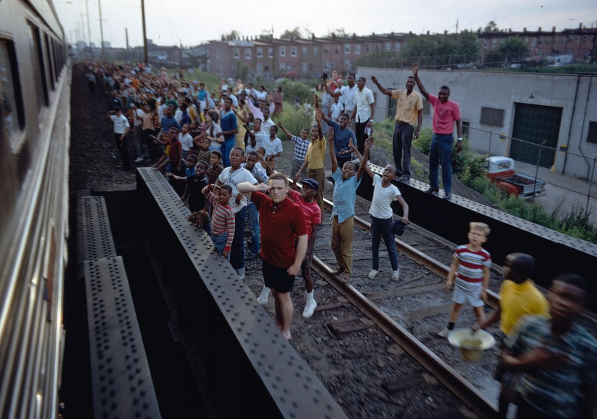 #19 People wave and salute as Robert F. Kennedy’s funeral train travels past, rolling from New York City to Washington, D.C., on June 8, 1968