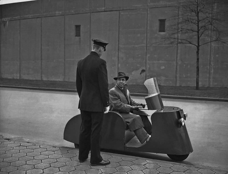 #8 A man sitting on a three-wheeled ‘Motorette’ scooter.