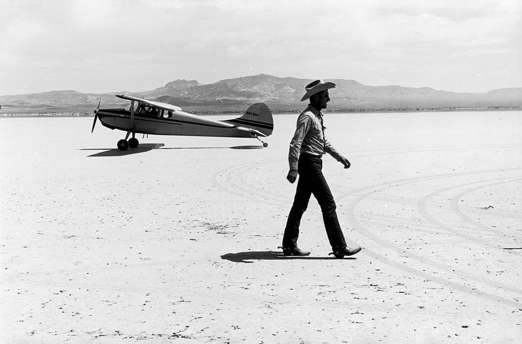 A man walking in front of a small aircraft on location in the Nevada Desert, during the filming of John Huston’s ‘The Misfits’.