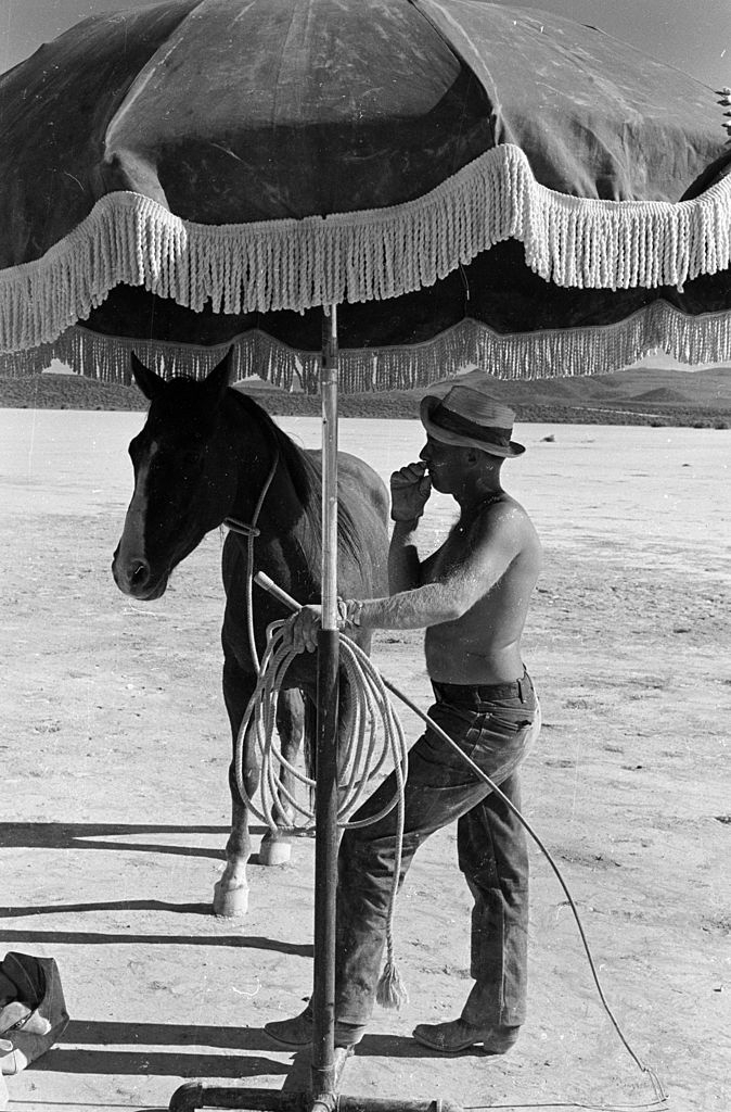 A trainer with a whip shares his shade with a horse on the set of John Huston’s ‘The Misfits’