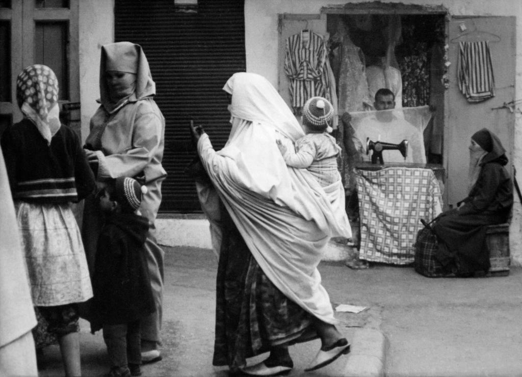 #79 Women in the street pass by a tailor’s workshop in the Medina on April 6, 1968 in Rabat, Morocco.