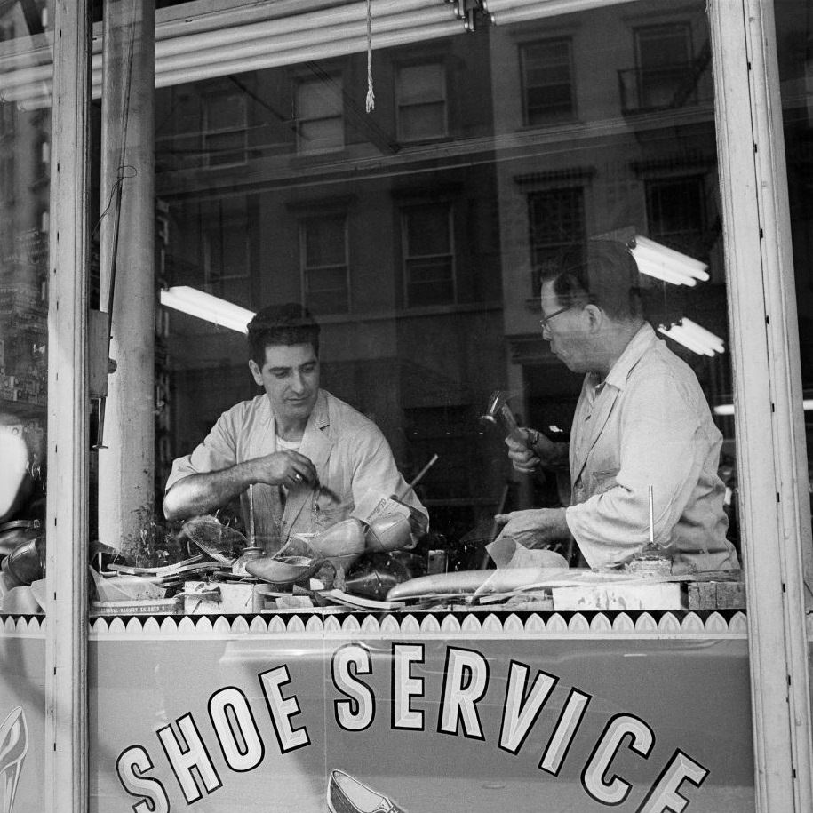 #57 Two cobblers work inside a shoe repair store in Brooklyn Heights, March 1958.