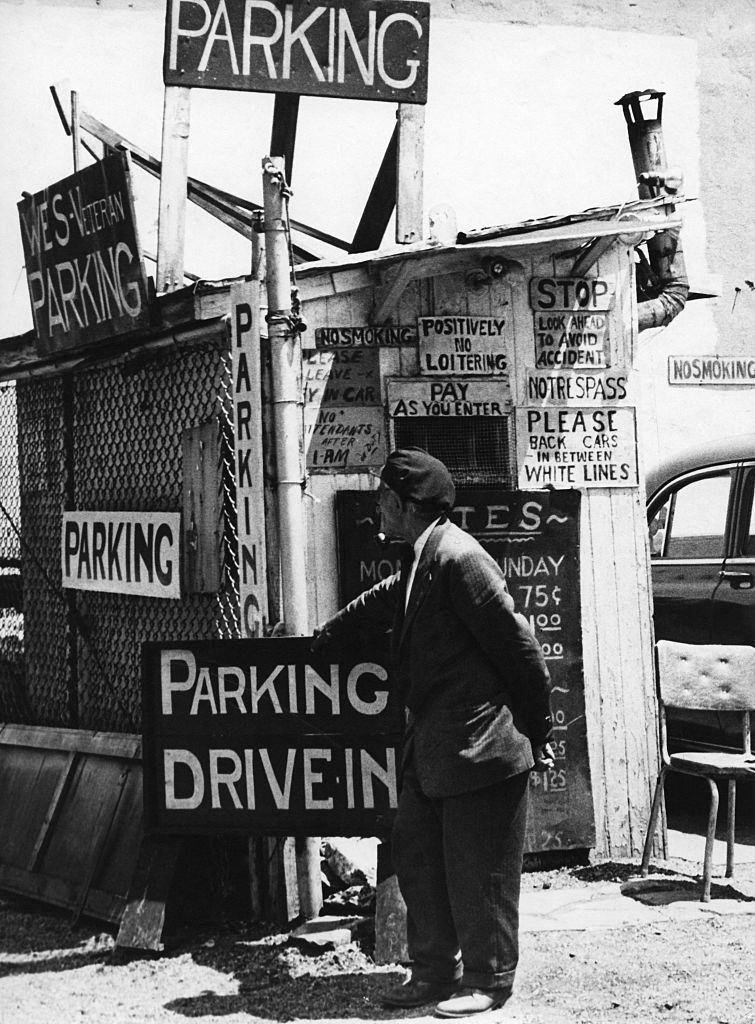 #59 A car park attendant stands by his hut among many signs in Brooklyn Heights, March 1958.