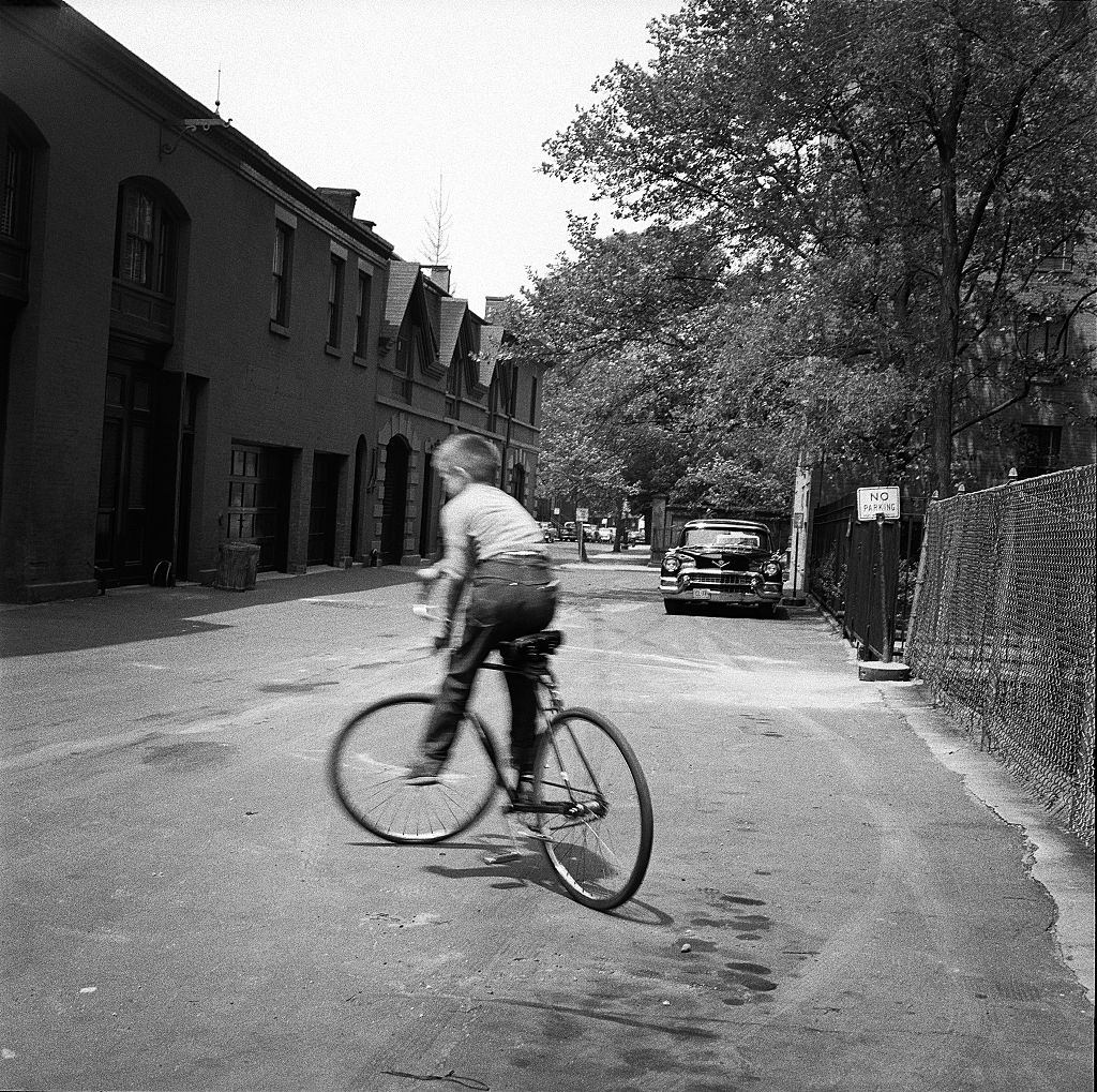 #73 A young boy rides his bicycle in the street in Brooklyn Heights, March 1958.