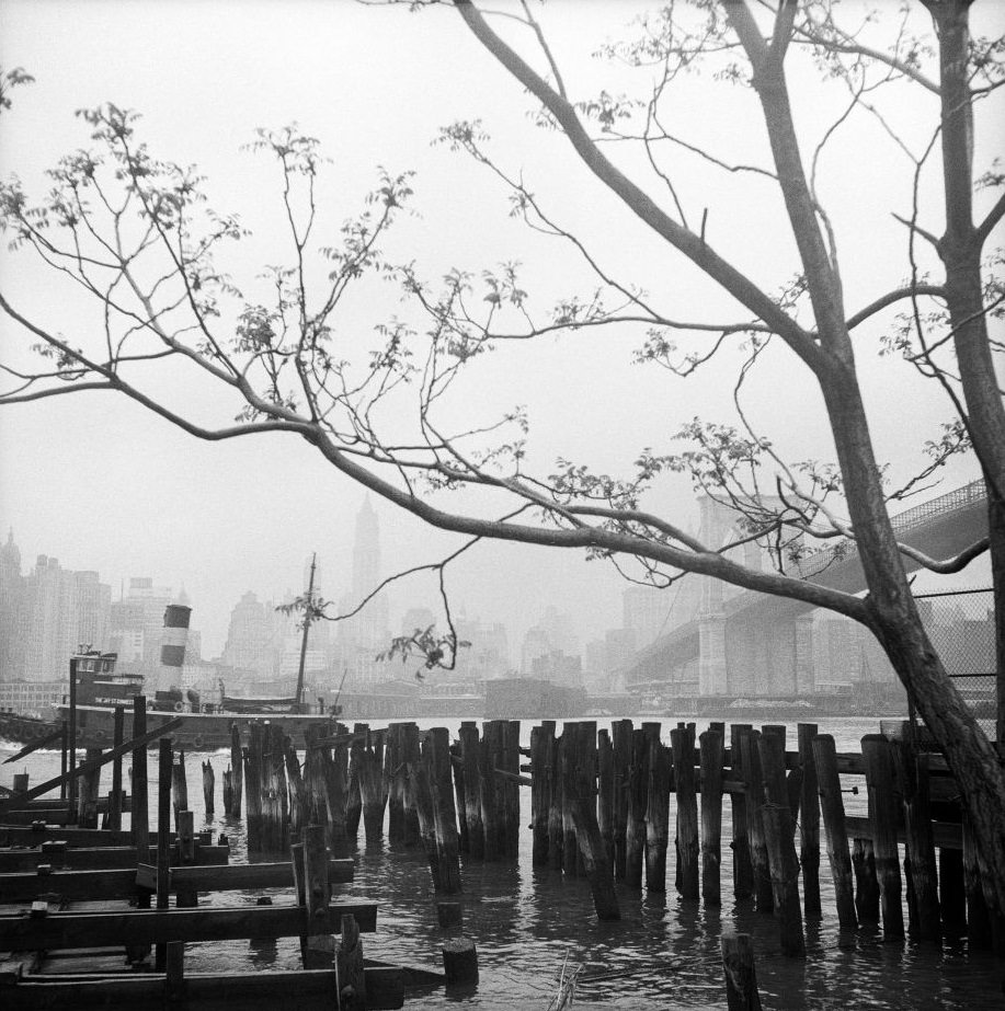 #64 A view of the Brooklyn Bridge and the Manhattan skyline from the waterfront in Brooklyn Heights, March 1958.