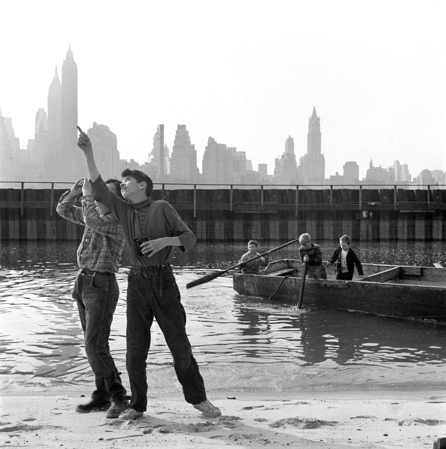 #26 Kids play near and in the East River with a view of the Manhattan skyline in Brooklyn Heights, March 1958.