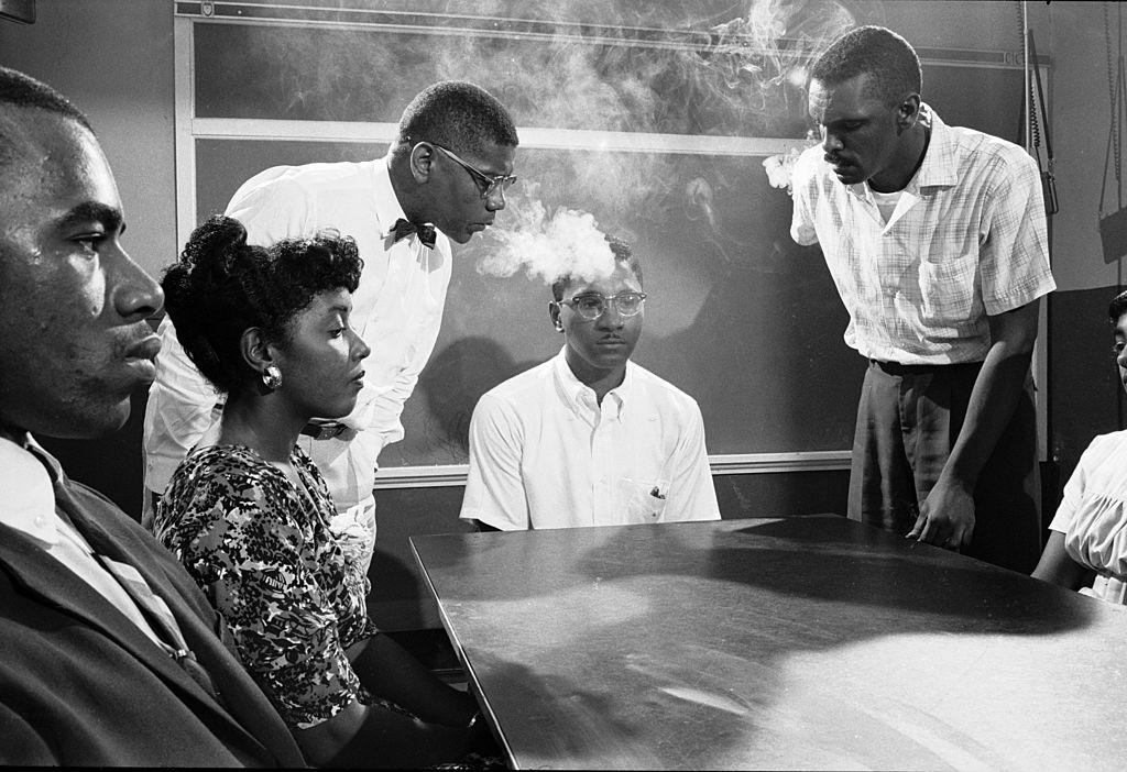#4 NAACP student advisor David Gunter (standing left) and Leroy Hill (standing right) blow smoke into the face of Virginius Thornton.