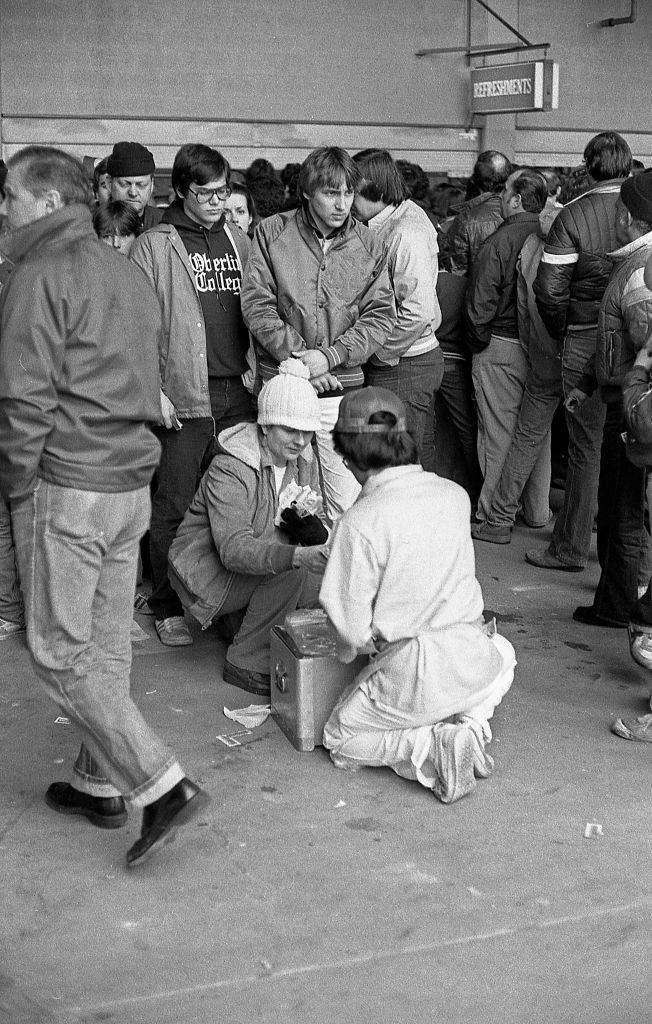 #24 A woman crouches down to purchase a hot dog from a vendor during an opening day baseball game at Shea Stadium. Queens, New York, 1982