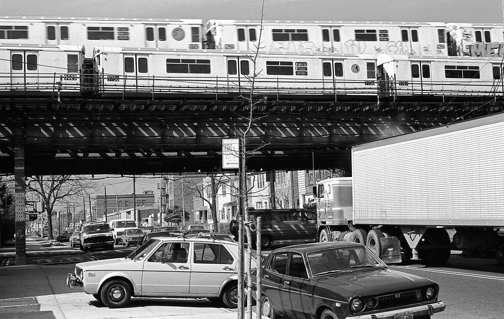 #18 Street traffic under the elevated subway tracks at the intersection of 108th Street and Roosevelt Avenue in Corona. Queens, New York, 1982.