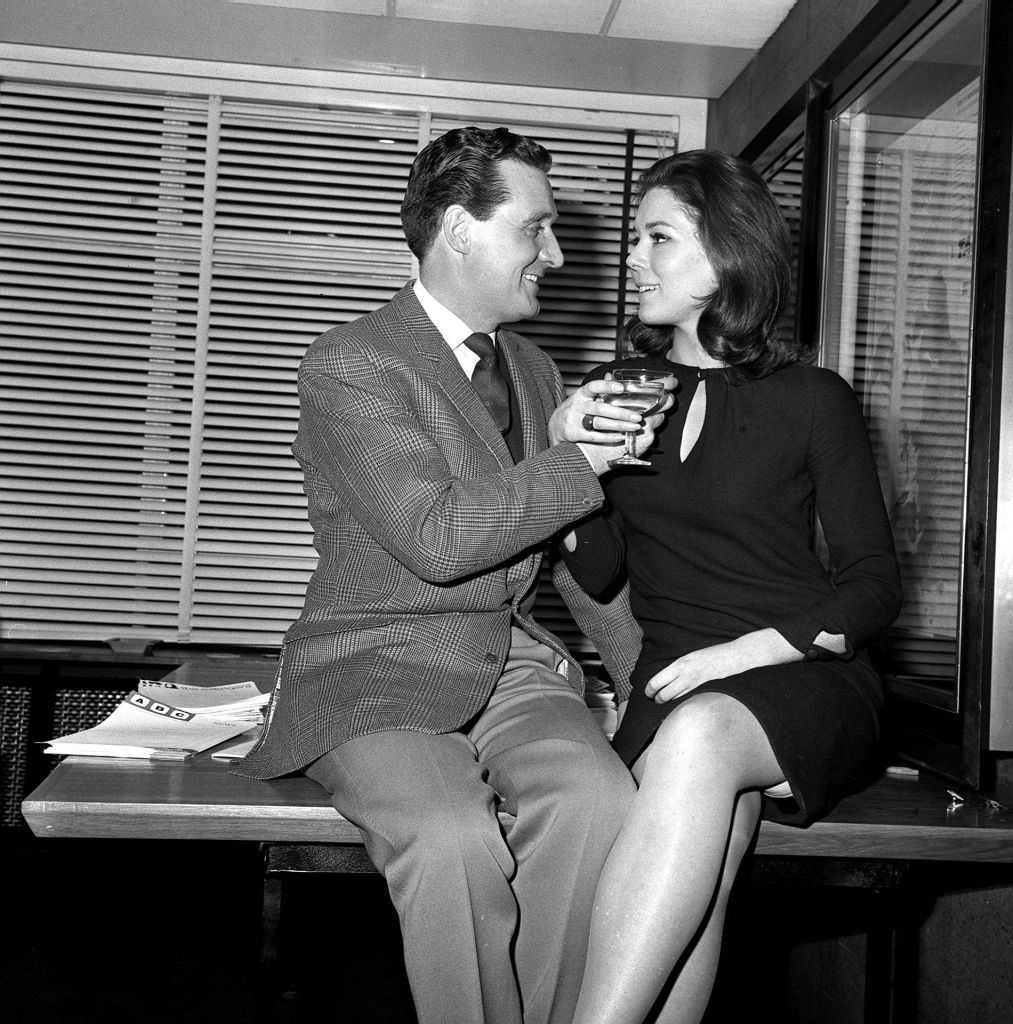 #15 Diana Rigg and Patrick Macnee sitting on a table, 1965.
