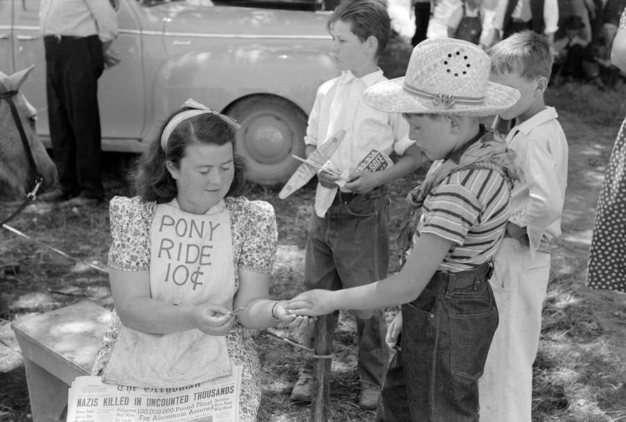 #22 Ticket taker for pony ride concession. The headline on the Oregonian in her lap reads “Nazis Killed in Uncounted Thousands – Berezina River Runs With Blood.”