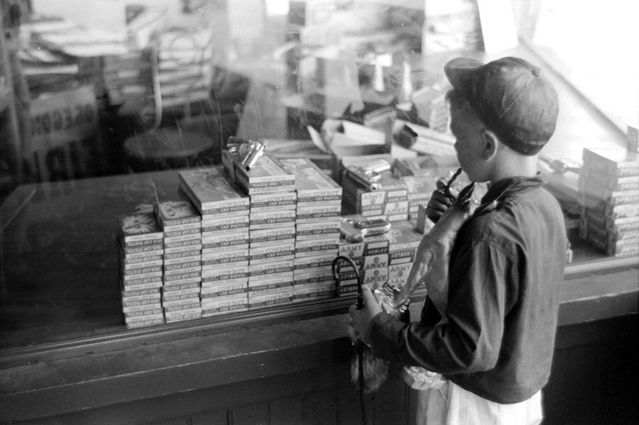 #7 A boy looks in a store window at Hubley brand cap guns, in ‘Army’, ‘Dick’, and ‘Cowboy’ models, on the fourth of July in Vale.