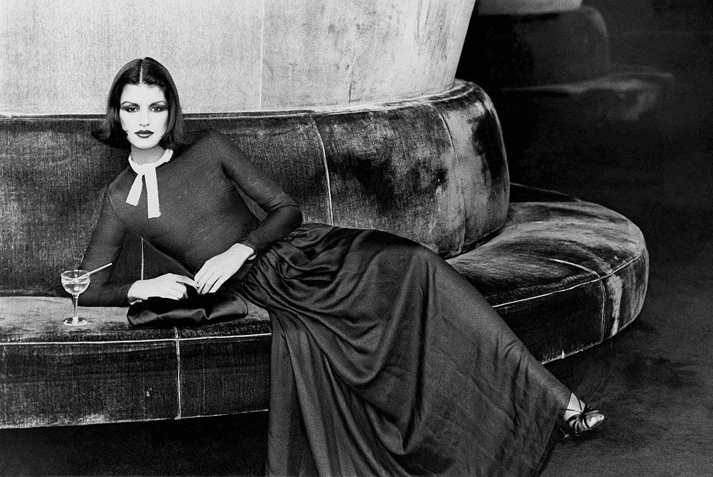 #4 Janice Dickinson, seated on circular banquette with a cocktail drink. Vogue, 1975.