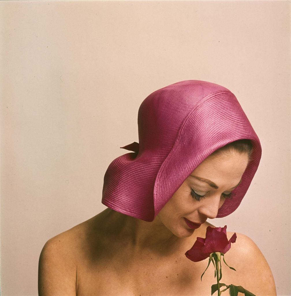 #36 Jean Patchett in a pink hat, looks down at a pink rose, 1961.