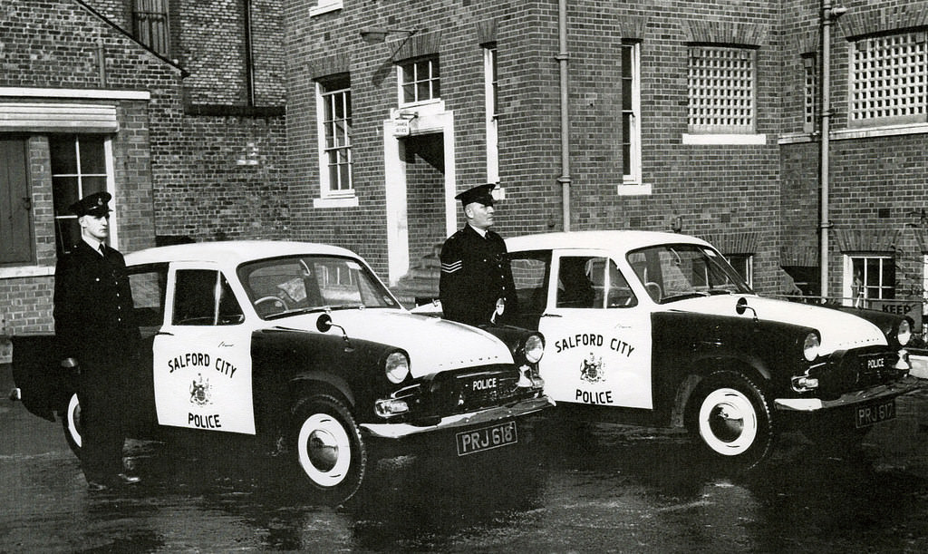 #29 Salford City Police officers proudly display their Hillman Minx patrol cars in the rear yard of their headquarters building in central Salford around 1960.