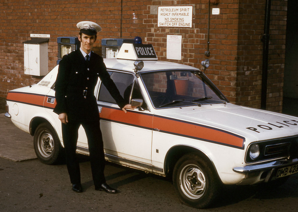 #45 A police officer stands proudly beside his Morris Marina police car in the yard of Stretford Police Station sometime in the mid 1970s