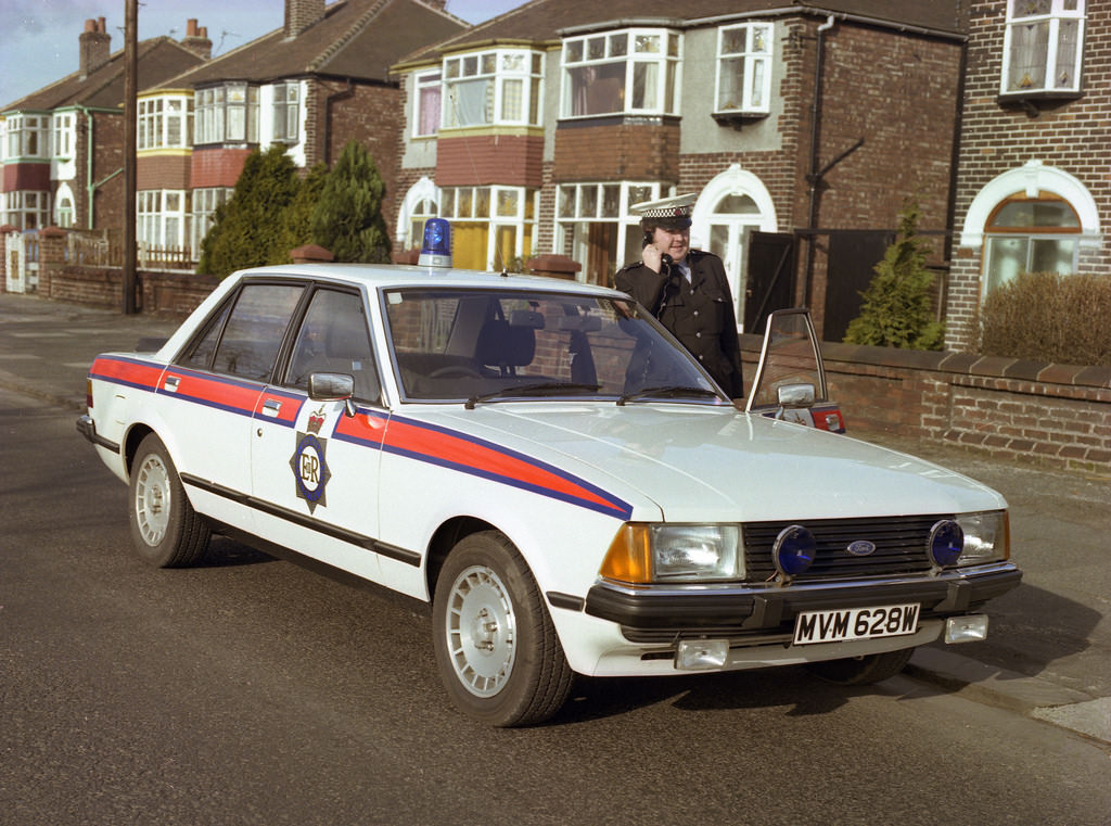 #59 A Greater Manchester Police traffic officer poses with his Ford Granada in the early 1980s
