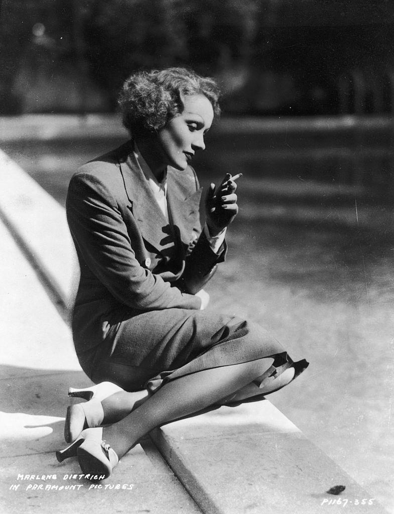 #24 Marlene Dietrich kneeling by a lake smoking a cigarette in a double breasted suit, 1932.