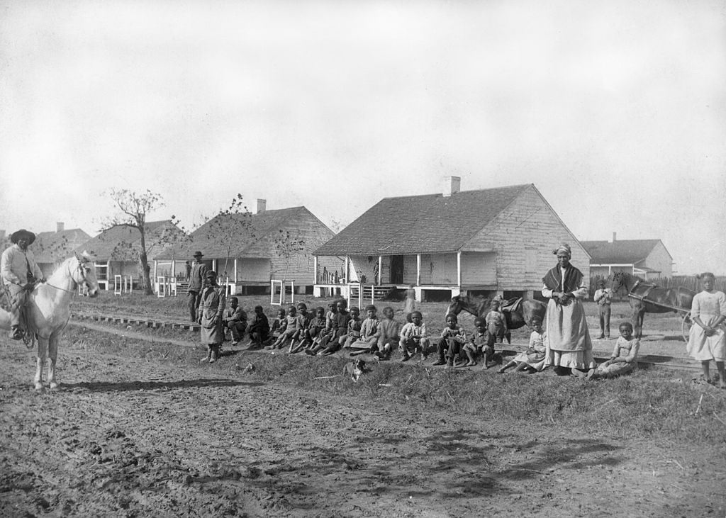 #13 African-American children sit on the edge of a railroad by a dirt road, in a shantytown on the outskirts of New Orleans, 1880.