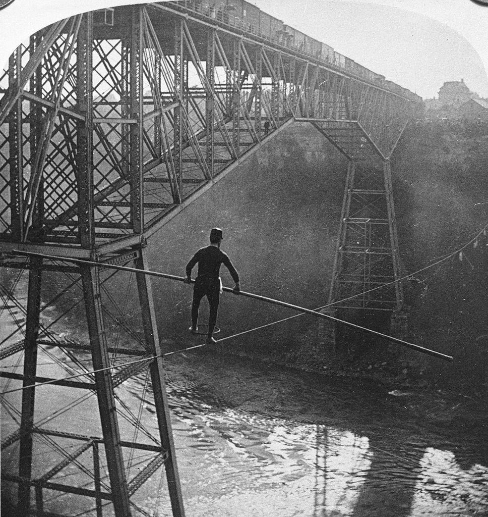 #19 Funambulist Samuel Dixon balances himself with a pole while using Stephen Peer’s cable to cross the Niagara Gorge towards Ontario,1890s.