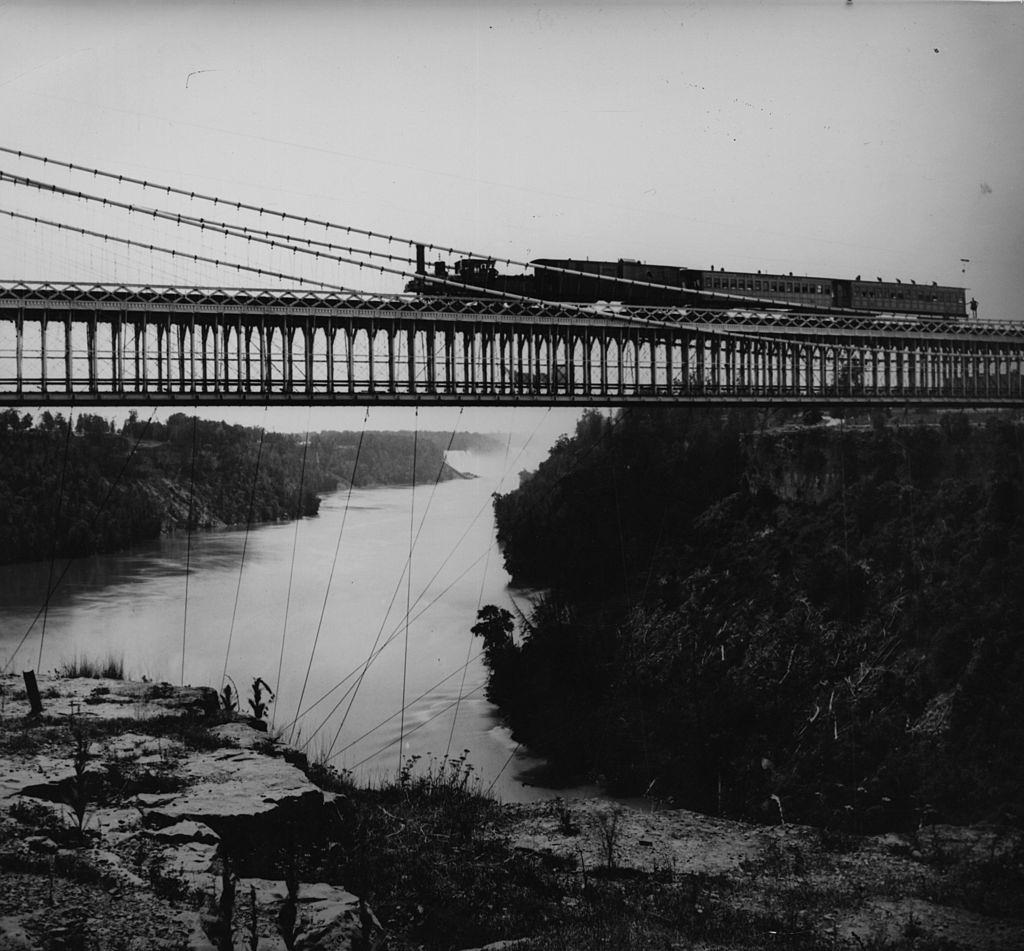 #27 A steam train crosses the Railway Suspension Bridge over the Niagara River, 1860s.