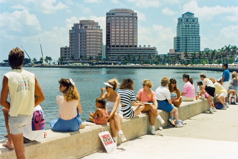 #29 People take a break at the Lake Worth seawall during F, with Phillips Point buildings in the background, 1990