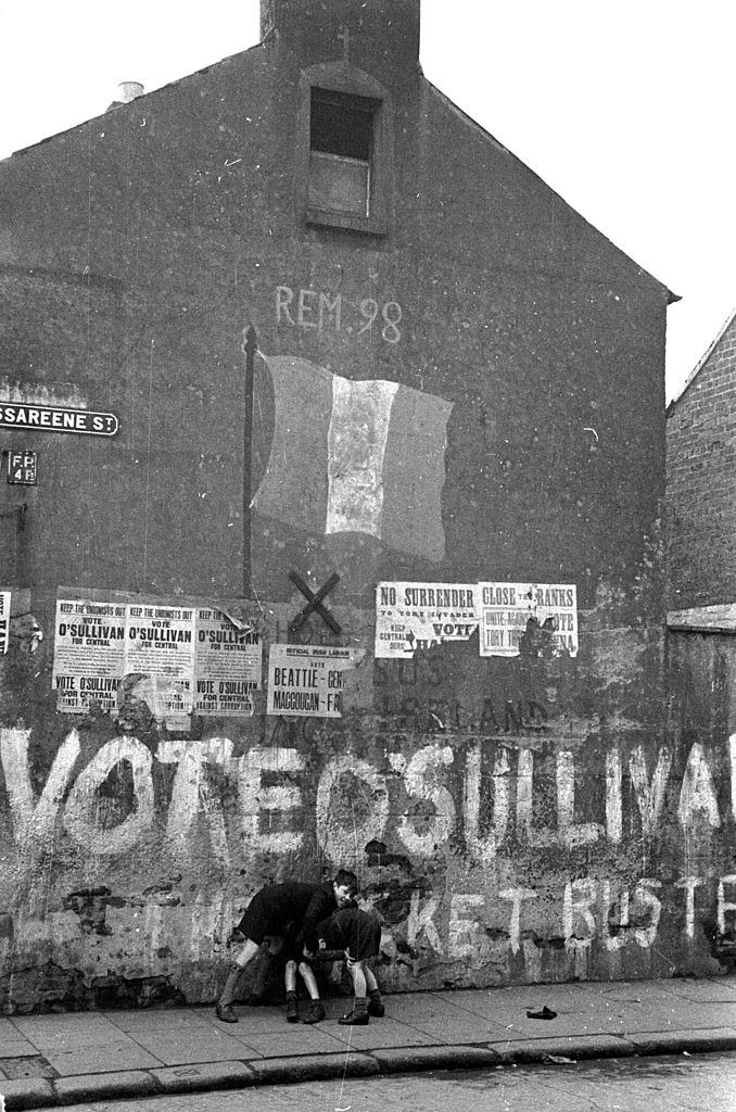 #29 Boys playing on a street in Belfast underneath a spray painted message supporting O’Sullivan in a local election, 1954.