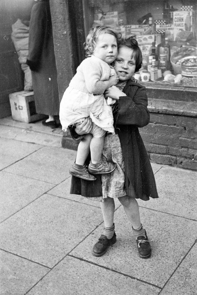 #30 A little girl looking after her younger sister on a street in Belfast, 1954.