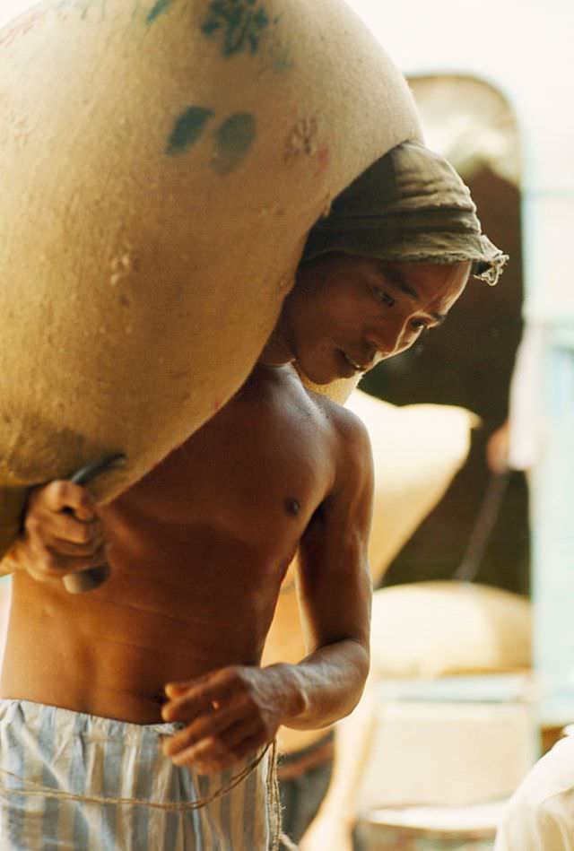 #14 A man carries a large bag of rice on his back, Cholon, in Saigon, 1961