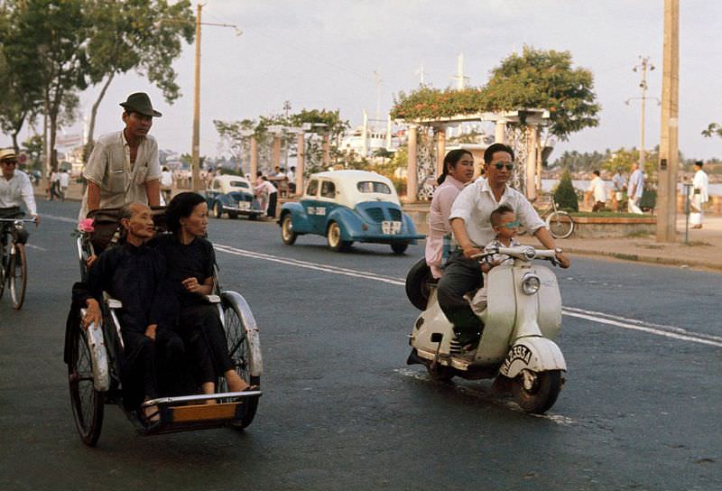 #9 A man drives his wife and son on a scooter past passengers on a cyclo in Saigon, 1961