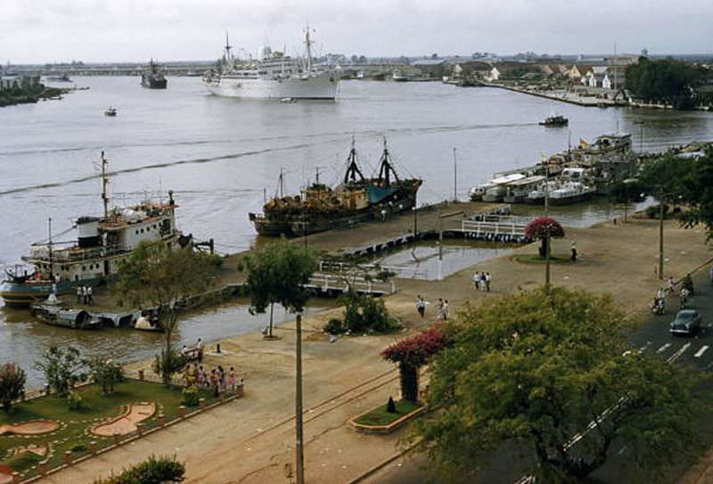 #30 People promenade along the waterfront as large ships sail into port in Saigon, 1961