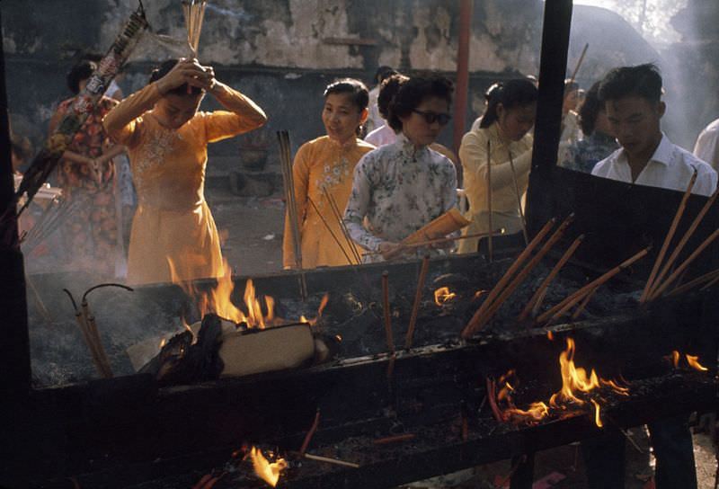#37 Women bow and pray by a fiery incense burner outside a temple in Saigon, 1961