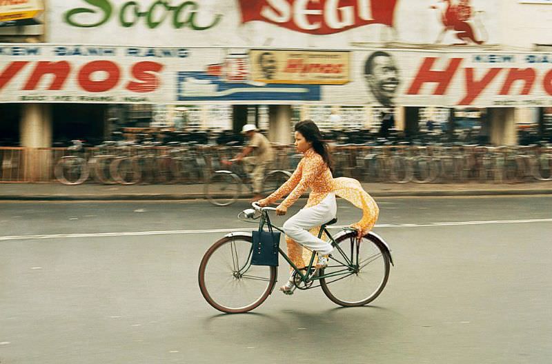 #2 A woman ties down her ‘Ao dai’ while riding her bicycle in Saigon, 1965