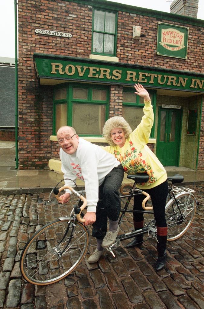 #61 Julie Goodyear and Roy Barraclough pictured on a tandem bike on the set of Coronation Street, 13th February 1990.