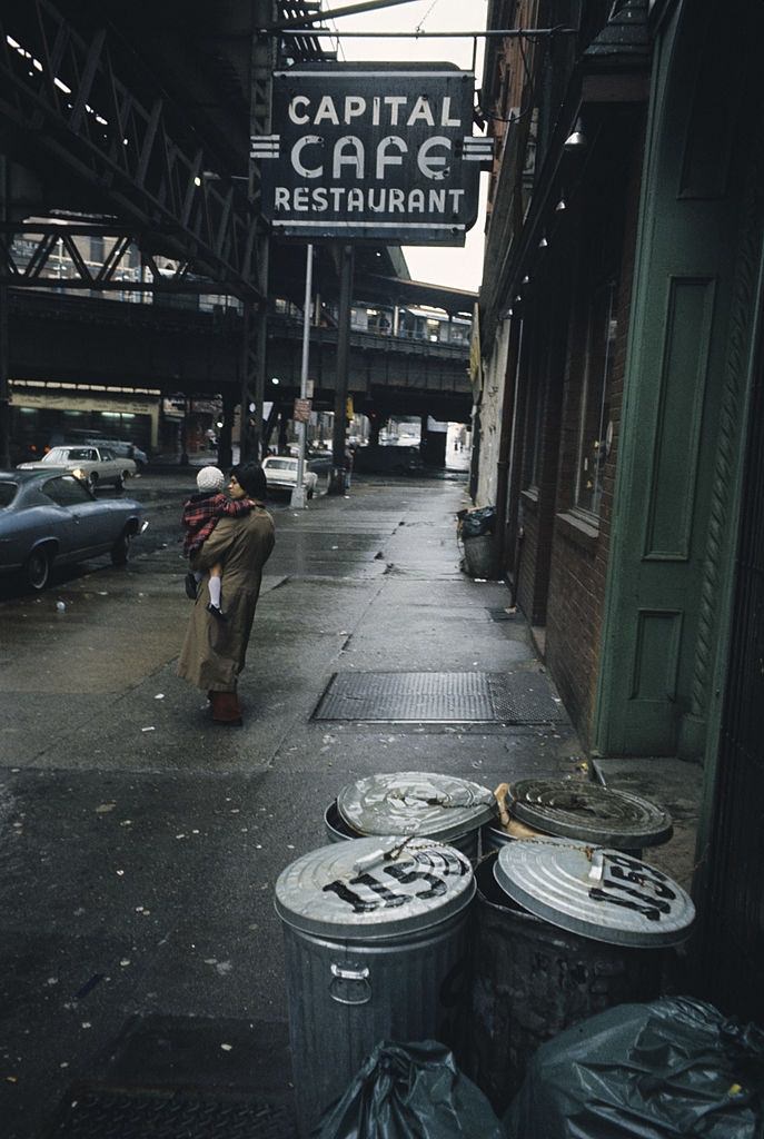 #32 A street overhung by bridges, on a sidewalk, near the front of a cafe, Brooklyn, 1973.