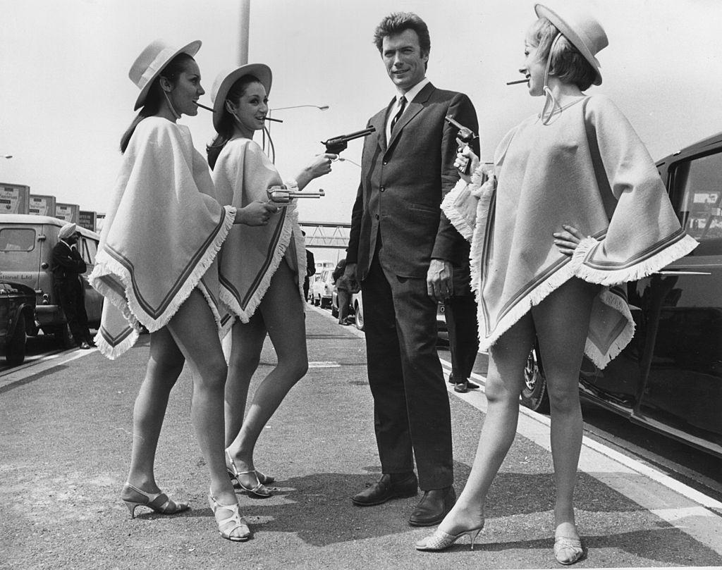 #50 Clint Eastwood with three gun-toting gals upon his arrival at London Airport, 1967.