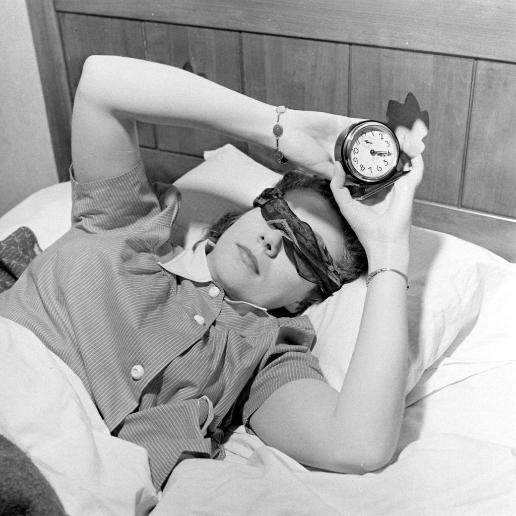 #13 Radio announcer Jean Ruth Hay holding an alarm clock while lying on the bed, Salt Lake City, 1942.