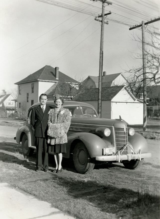 #12 A lady dressed in a fur coat and a fellow in a double-breasted suit posing with a 1937 Oldsmobile Eight on a sunny winter’s day.