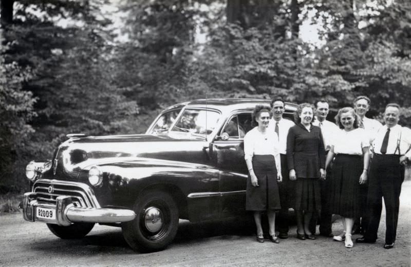 #16 Seven members of a Belgian middle-class family posing with a 1947 Oldsmobile in the countryside, 1948