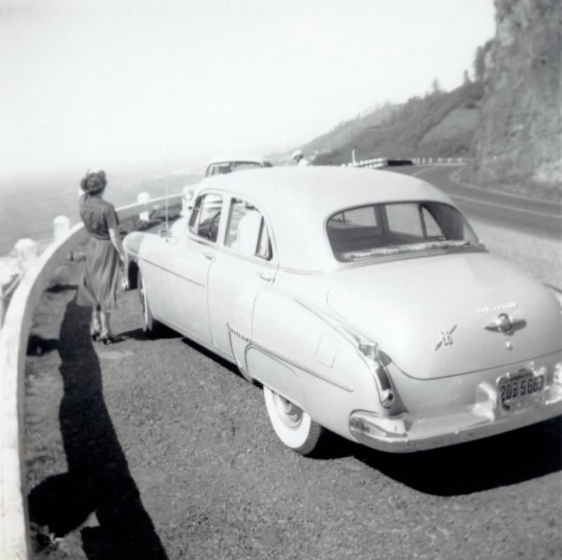 #23 A lady in a 3/4 length skirt enjoying the view from a vista point on a panoramic road overlooking the ocean.