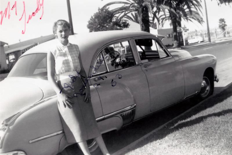 #27 A young blonde lady posing with a 1949 Oldsmobile 88 4-Door Sedan on a sunny day.