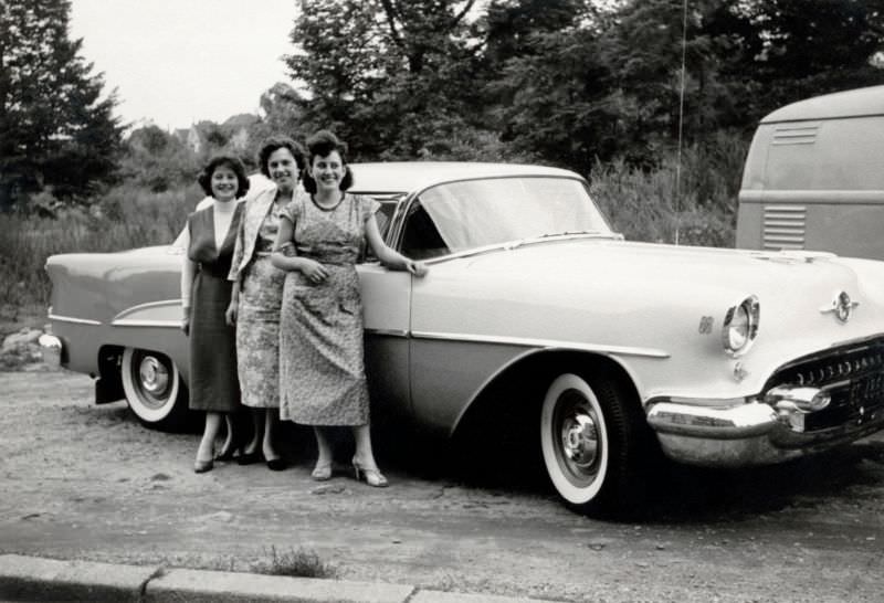 #28 Three cheerful ladies posing with a shiny two-tone 1955 Oldsmobile 88 in the countryside, 1955