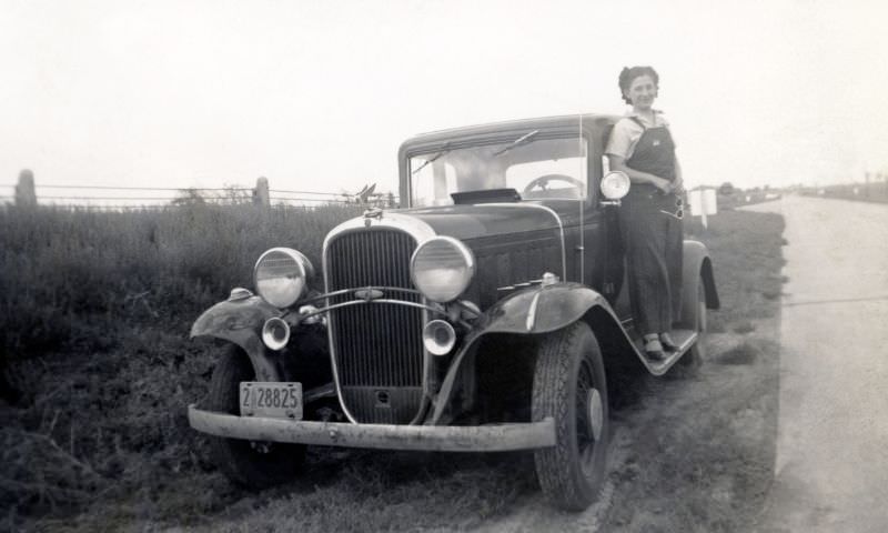 #8 A young lady in bib overalls posing on the running board of a 1932 Oldsmobile Eight in the countryside.