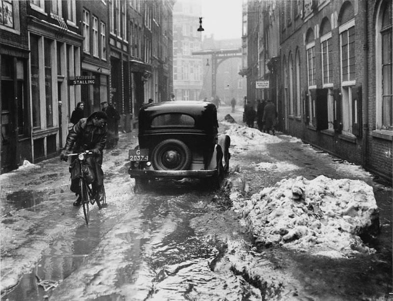 #29 Thaw in Amsterdam, car passes cyclist in the Staalstraat. Amsterdam, March 11, 1947